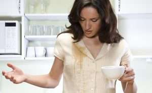 Young woman in kitchen, coffee spilit on shirt